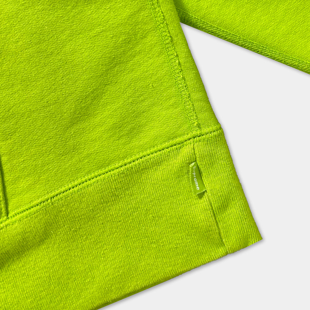 A close-up view of a bright green fabric, possibly a sweater or garment, with a small tag or label attached to the bottom right corner.