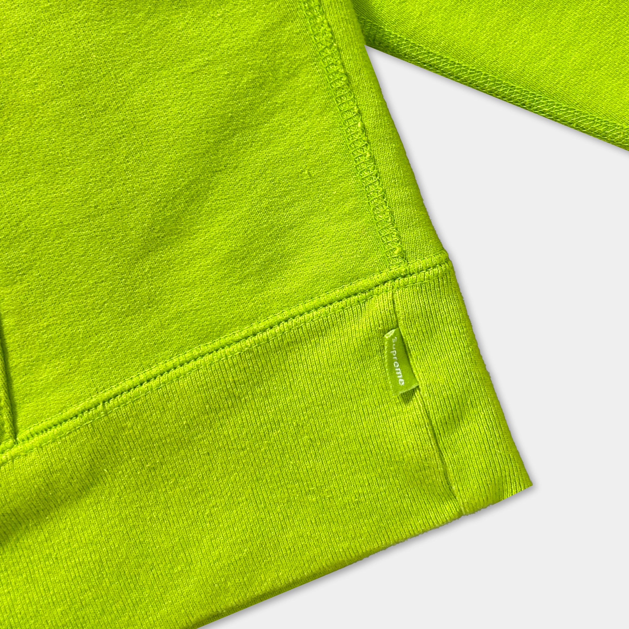 A close-up view of a bright green fabric, possibly a sweater or garment, with a small tag or label attached to the bottom right corner.