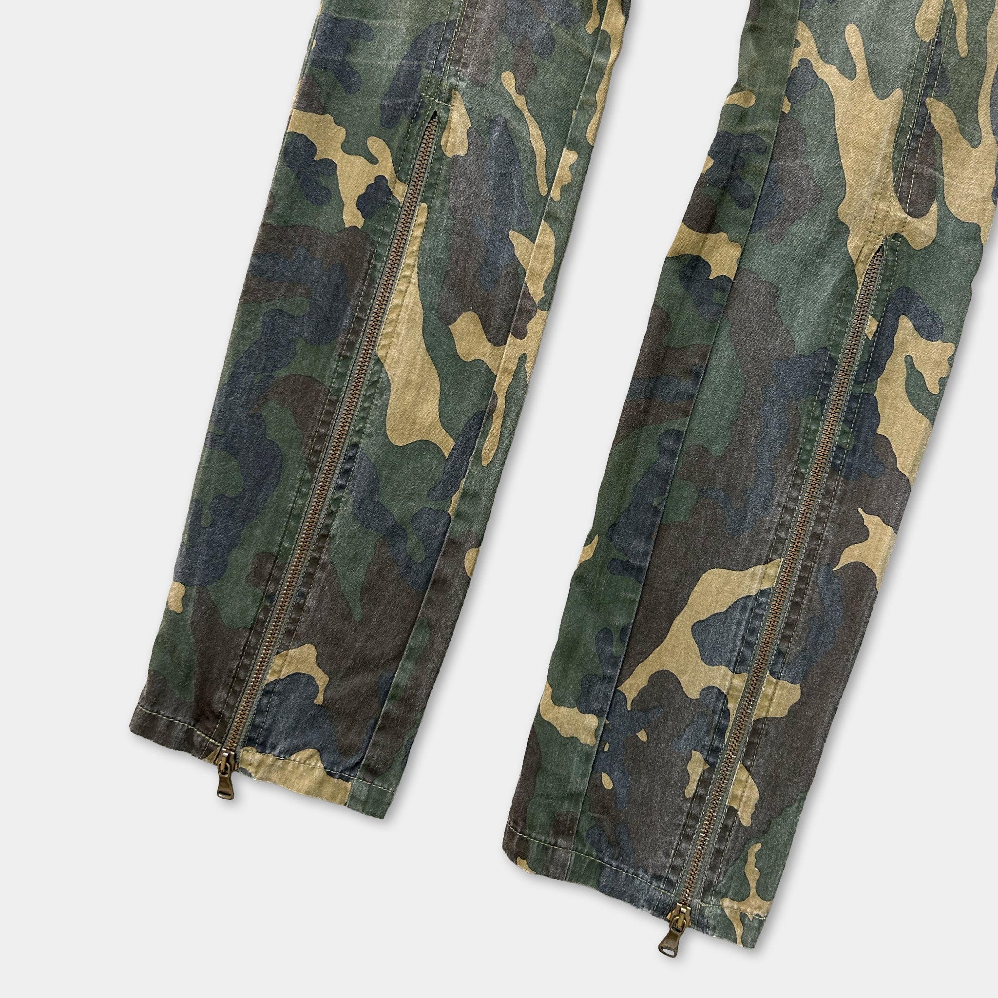 a pair of camouflage pants with zippers, featuring a distinctive pattern of green, brown, and black colors.