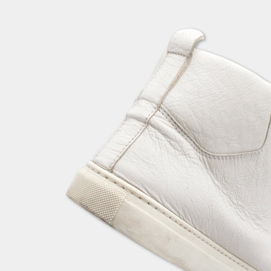 A close-up view of a white leather sneaker, showing the sole and heel of the shoe.