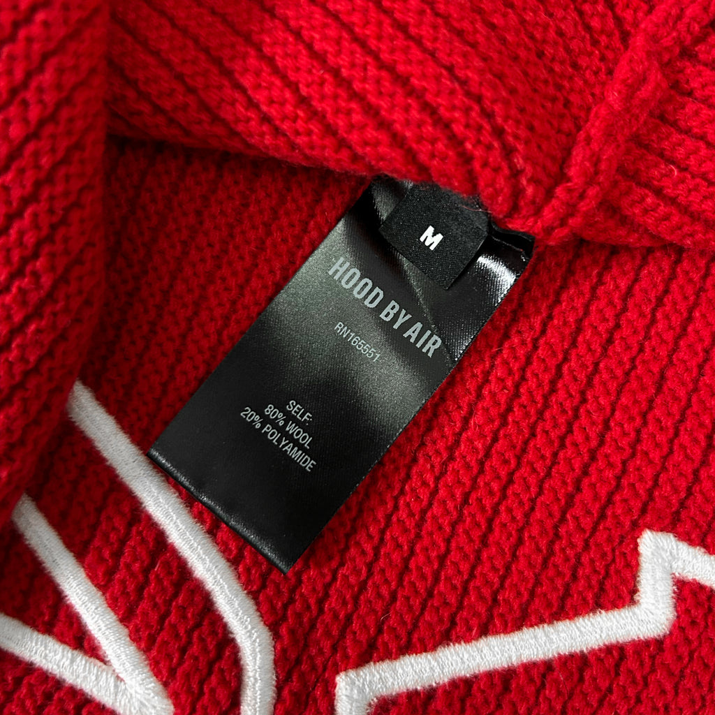 A close-up view of a red knitted sweater with a black label attached to it.