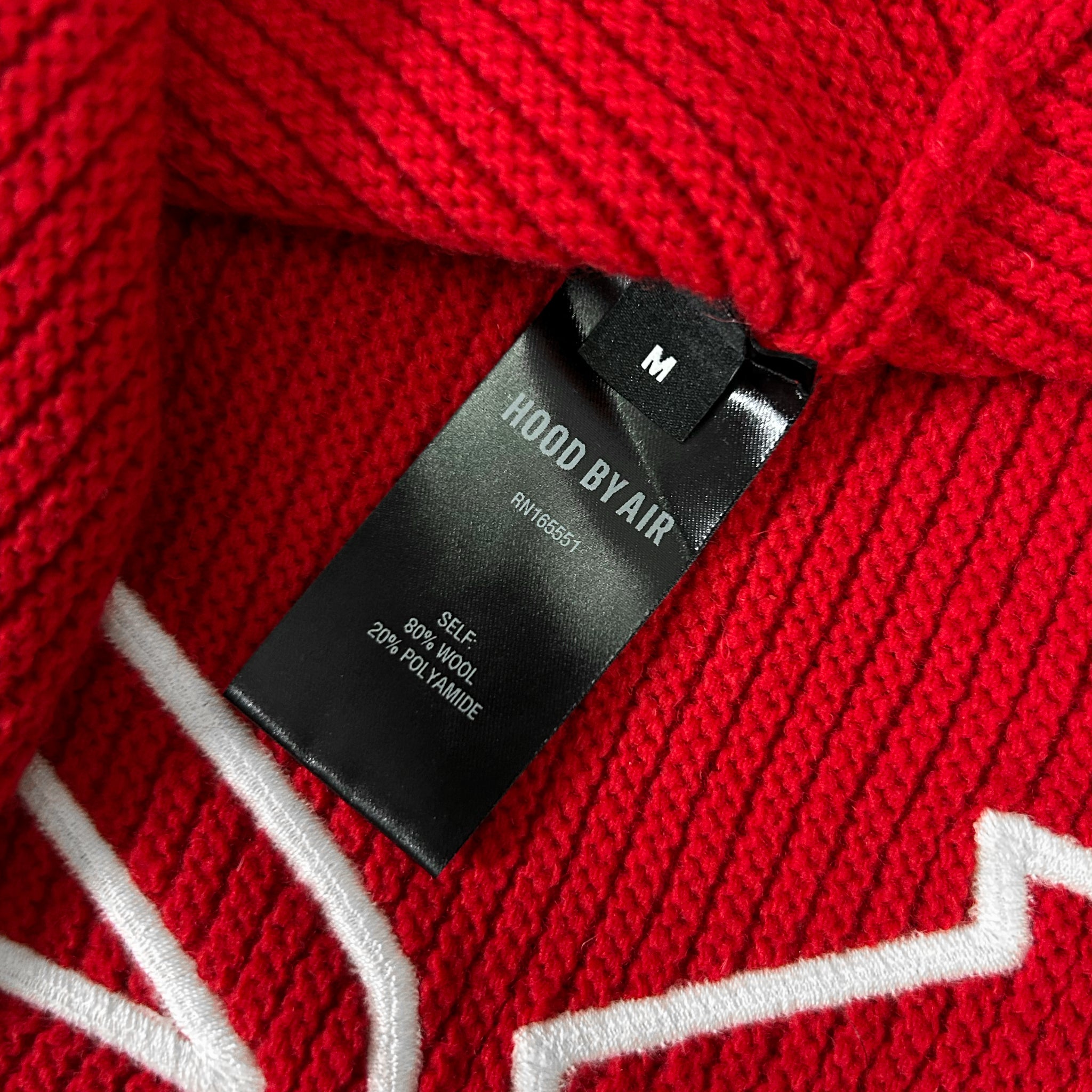 A close-up view of a red knitted sweater with a black label attached to it.