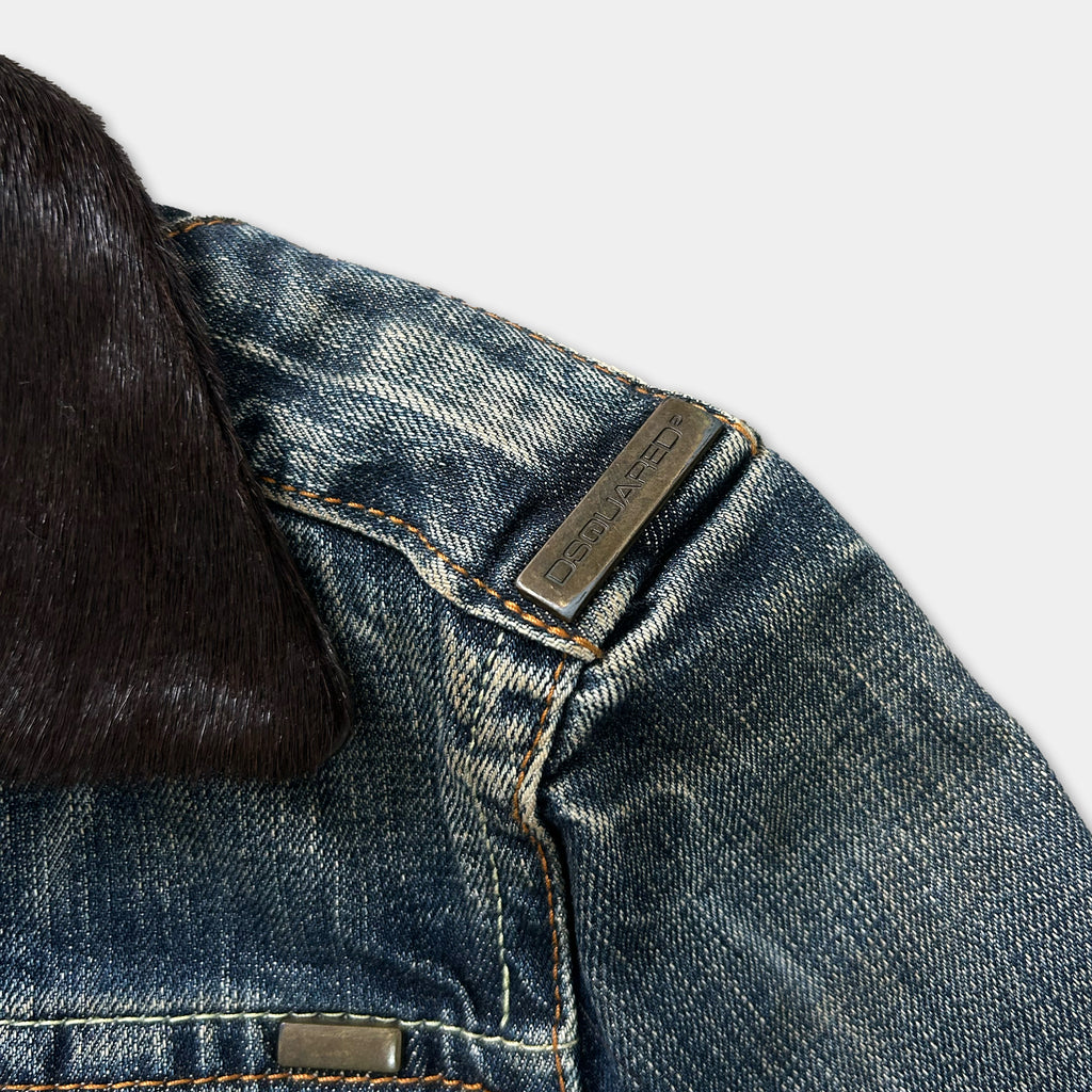 a close-up view of a denim jacket, focusing on the zipper and a metal tag attached to the jacket.