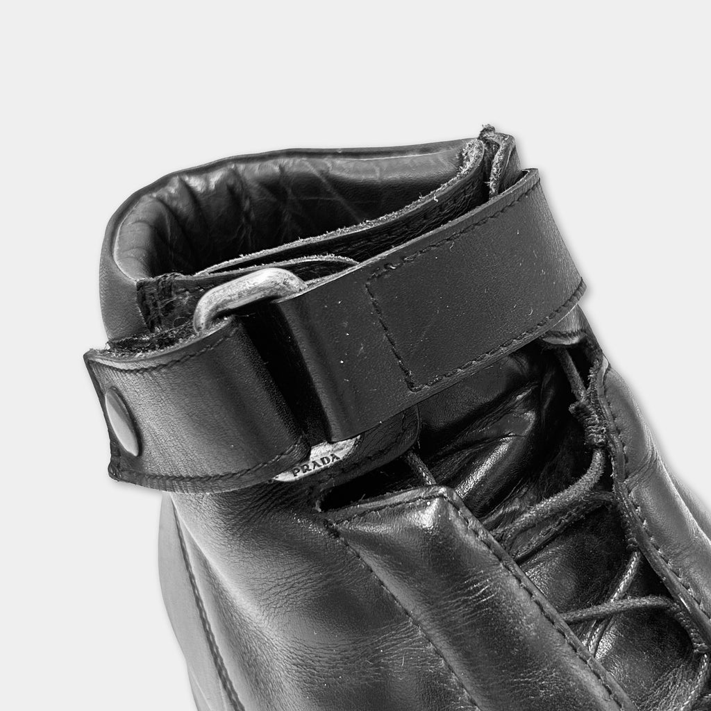 A close-up view of a black leather boot with a buckle and laces.