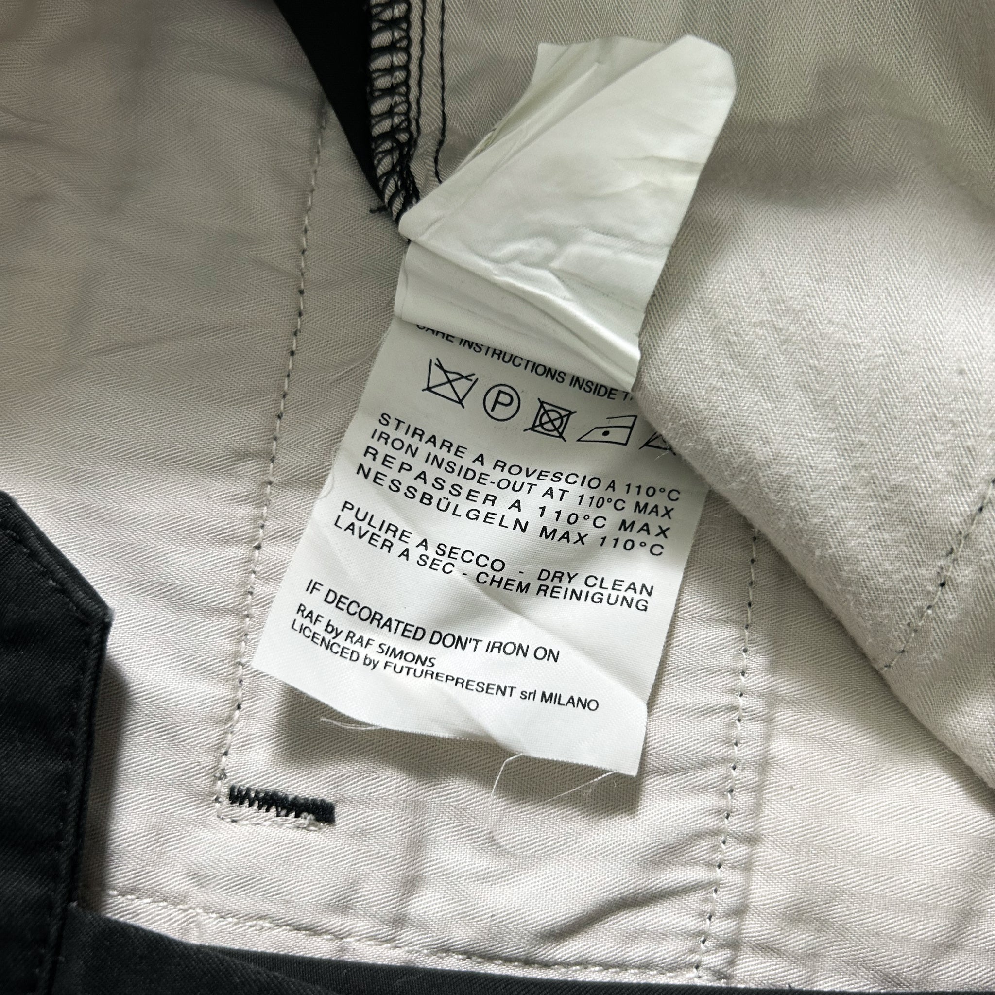 a close-up view of a white fabric label attached to a piece of clothing, with a black fabric visible on the left side.