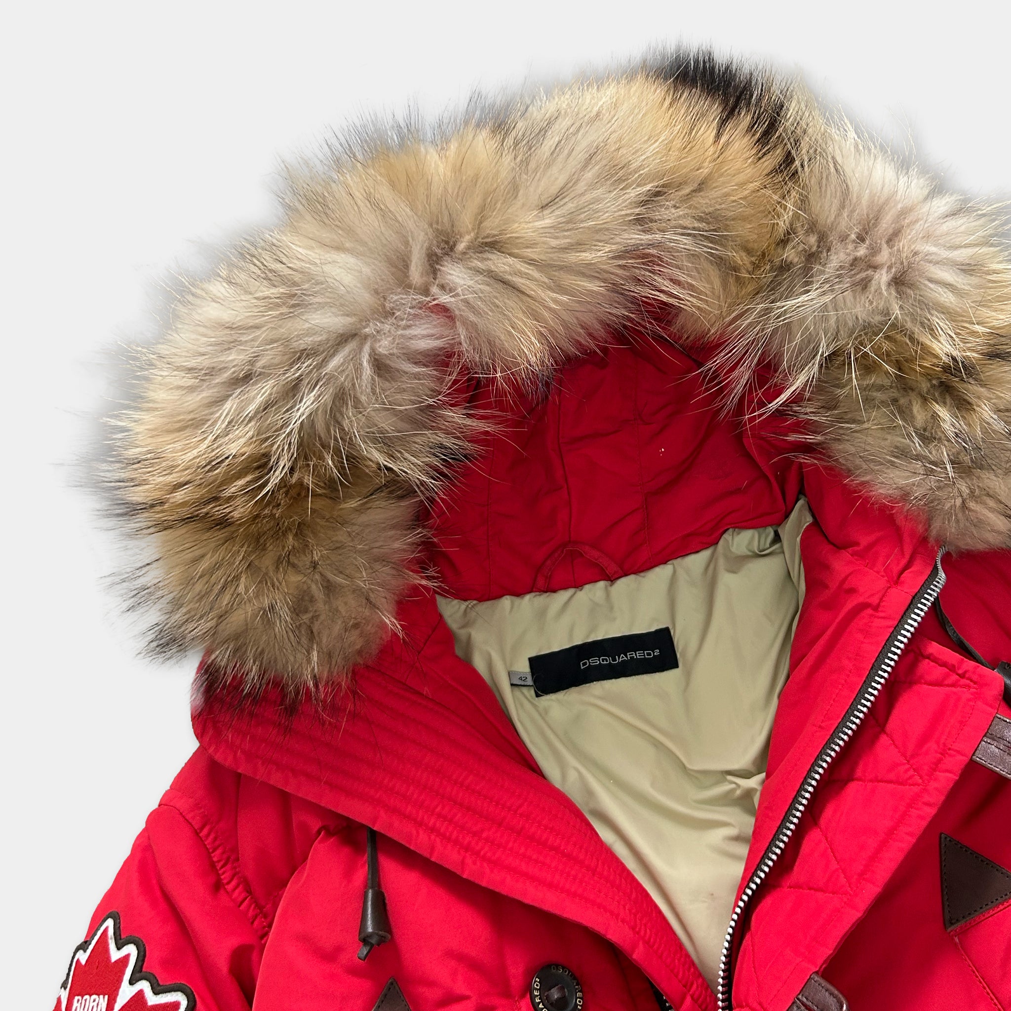 A close-up view of a red winter coat with a fur-lined hood and a white label on the chest.