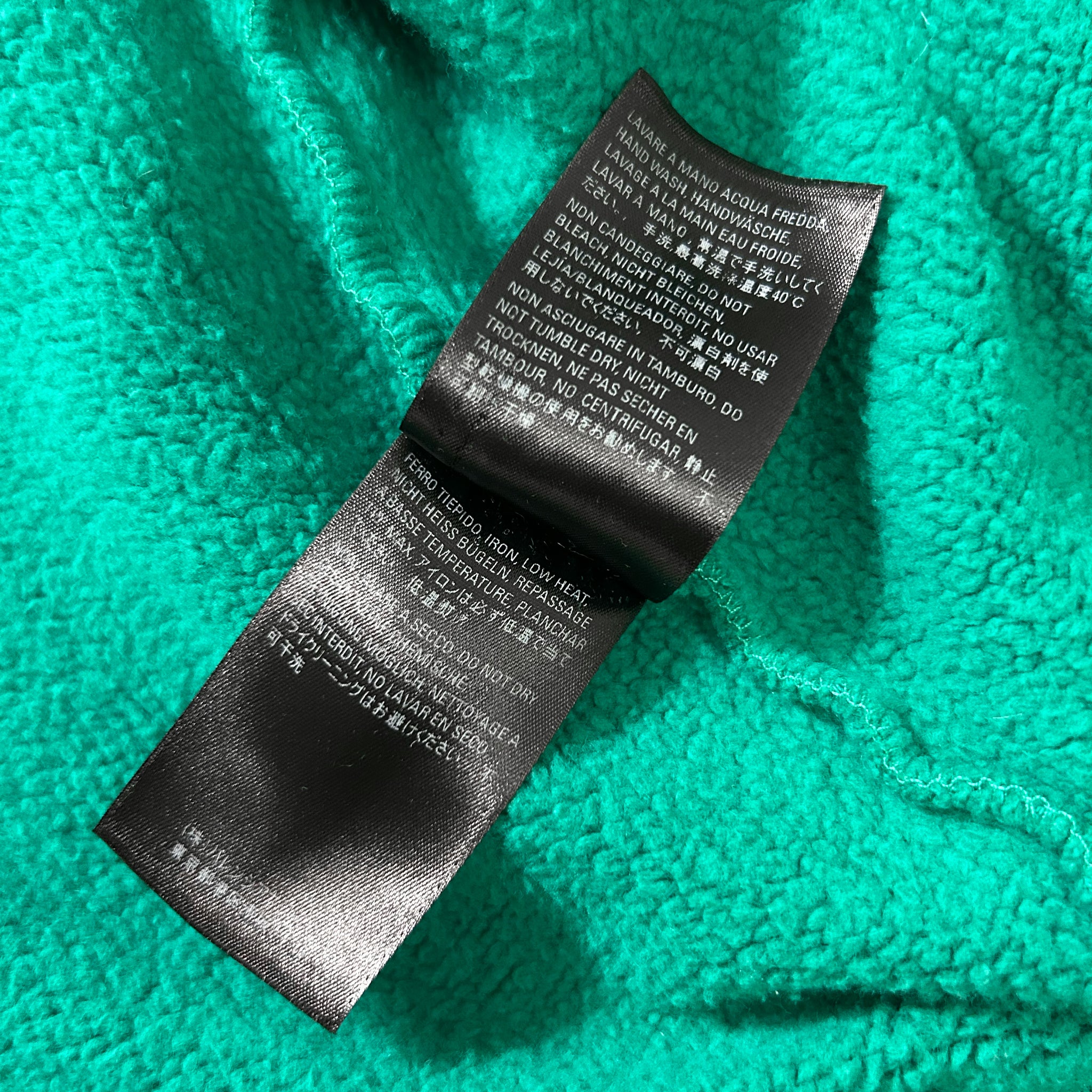a close-up view of a black fabric label with text on it, placed on a turquoise fabric background.