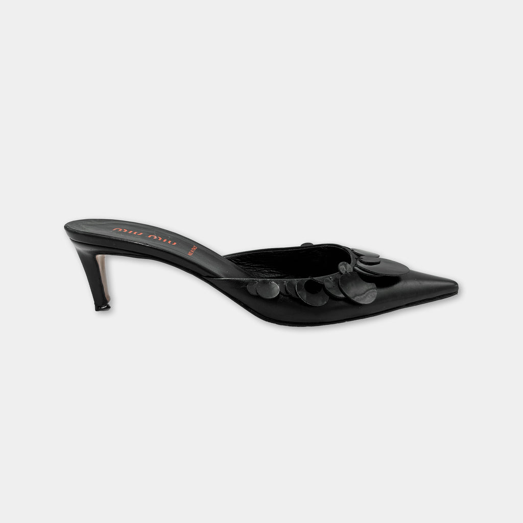 A black high-heeled shoe with a pointed toe and a decorative floral pattern on the side.