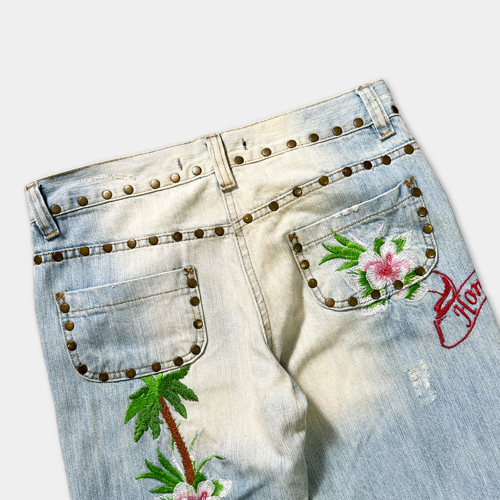 A pair of light blue denim jeans with decorative floral embroidery and metal studs on the waistband.