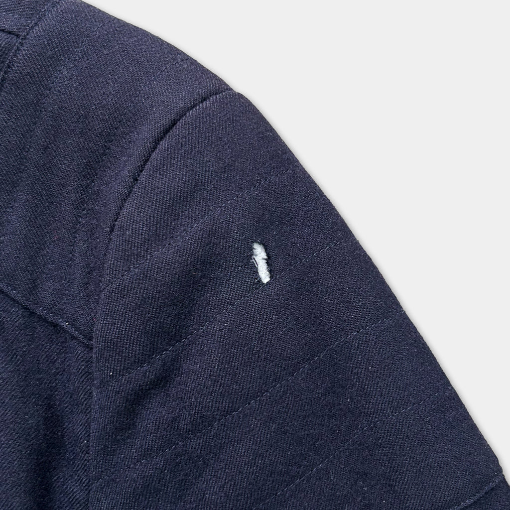 A close-up view of a dark blue fabric, possibly a jacket or sweater, with a small white tear or hole visible on the left side.