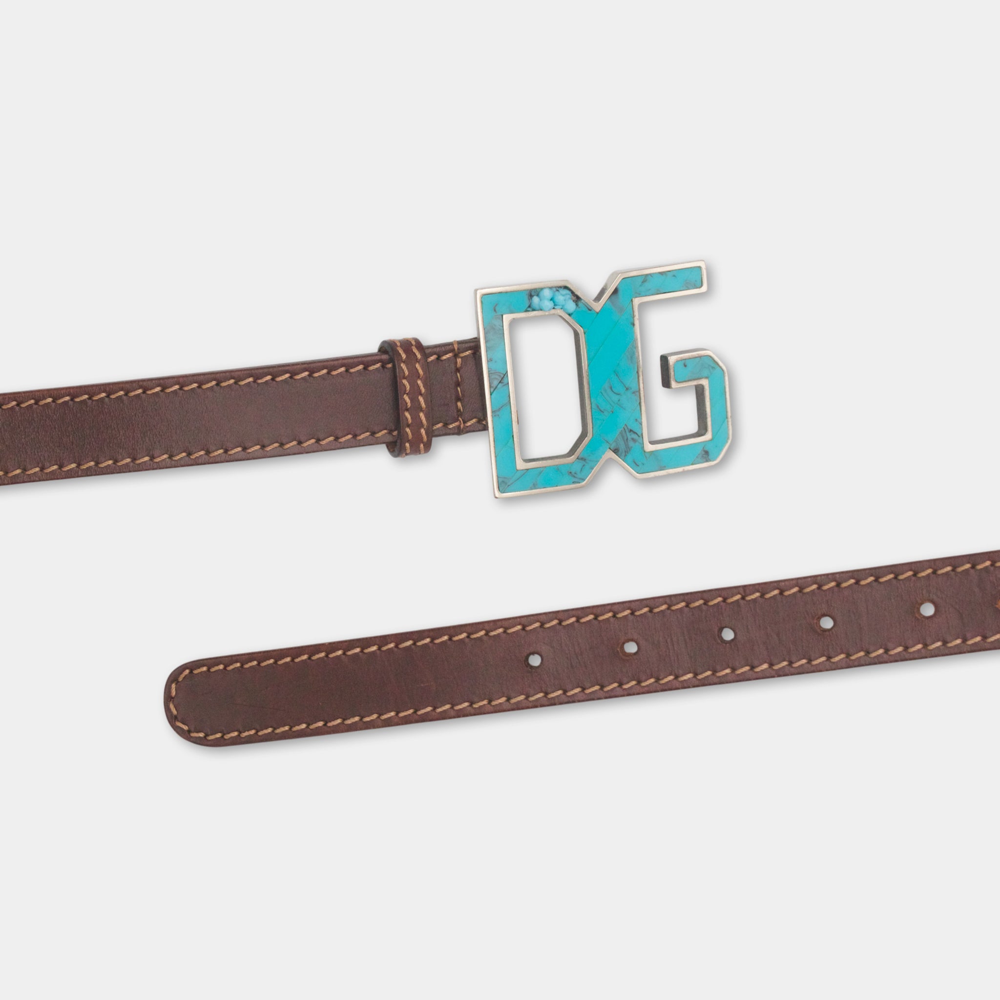 A brown leather belt with a turquoise-colored metal buckle featuring the letters 'DG' on it.