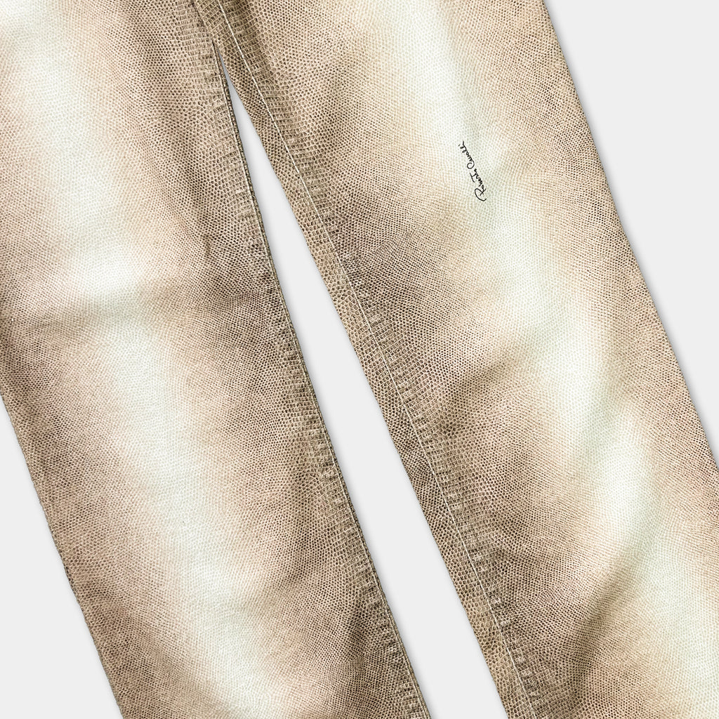 A close-up view of a pair of tan-colored jeans with a small black logo visible on the left leg.