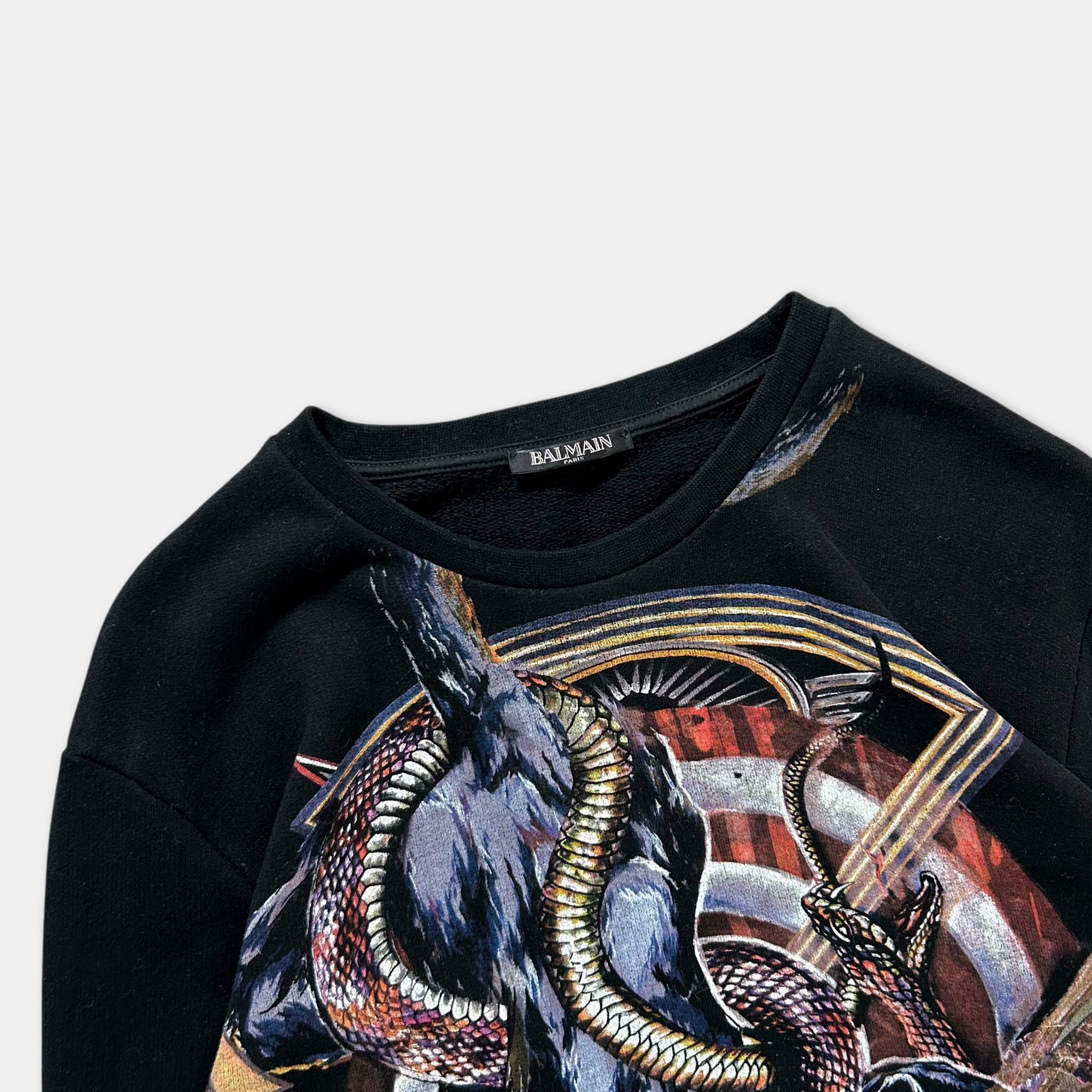 a close-up view of a black sweater with a colorful, intricate design featuring a large, detailed snake or cobra-like creature.