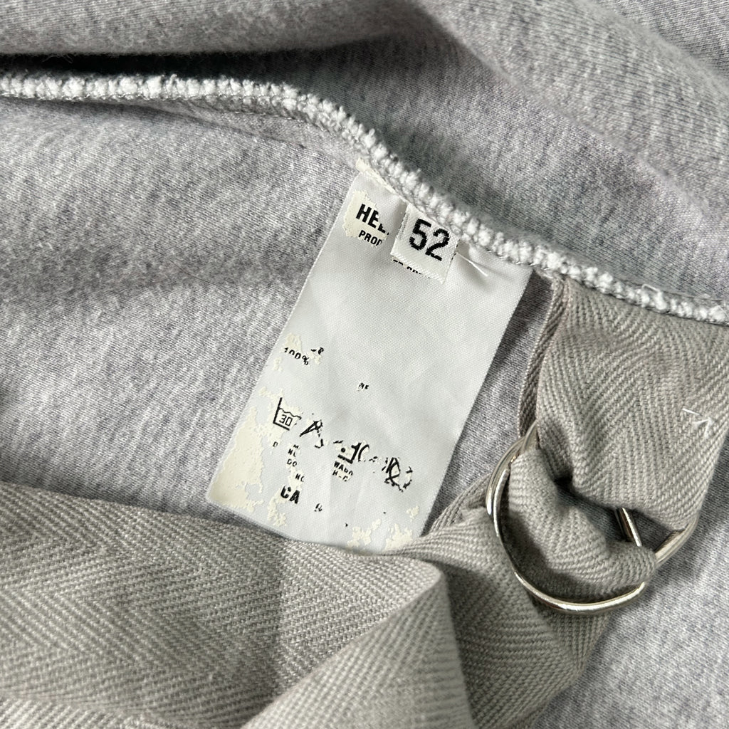 a close-up view of a grey fabric, possibly a sweater or garment, with a white label attached to it. The label appears to contain text and numbers, possibly indicating the product's details or measurements.