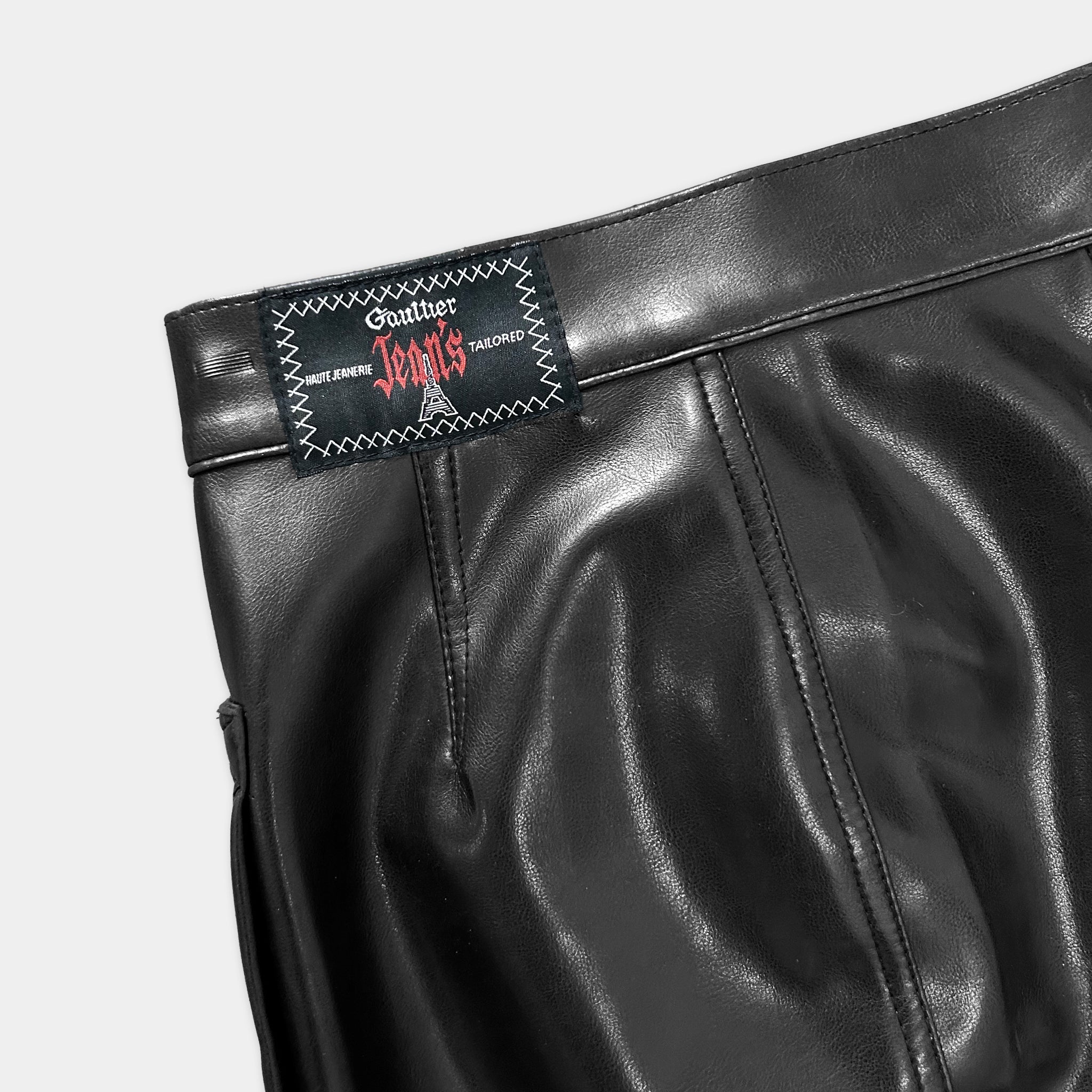 A close-up view of a black leather skirt or trouser with a label or tag attached to it.