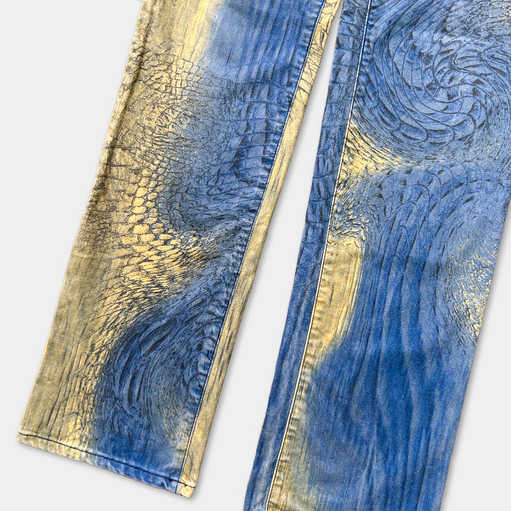 a pair of blue jeans with a unique pattern of blue and gold colors. The pattern appears to be a mix of abstract designs and textured elements, creating a visually striking and eye-catching appearance.