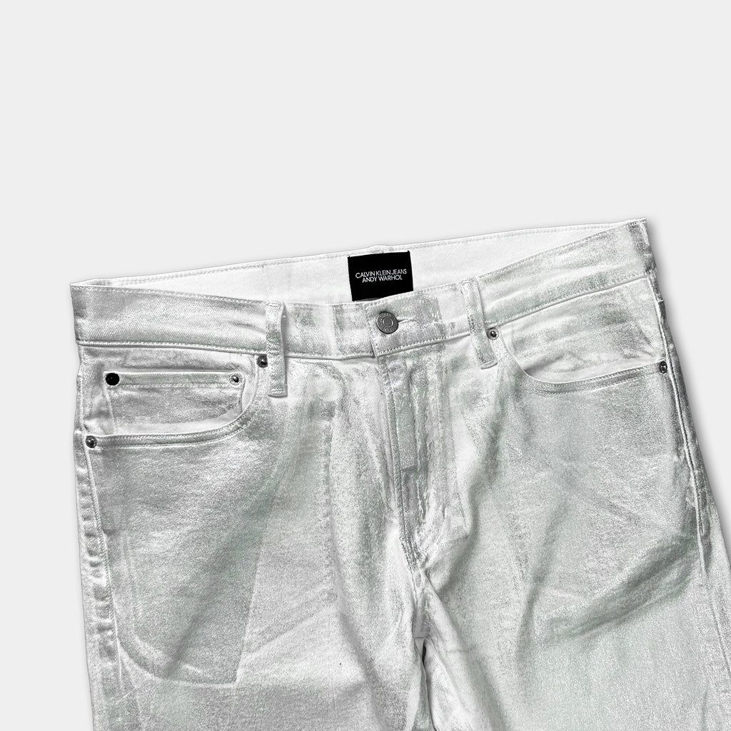 A pair of shiny, metallic silver jeans with a label on the waistband.