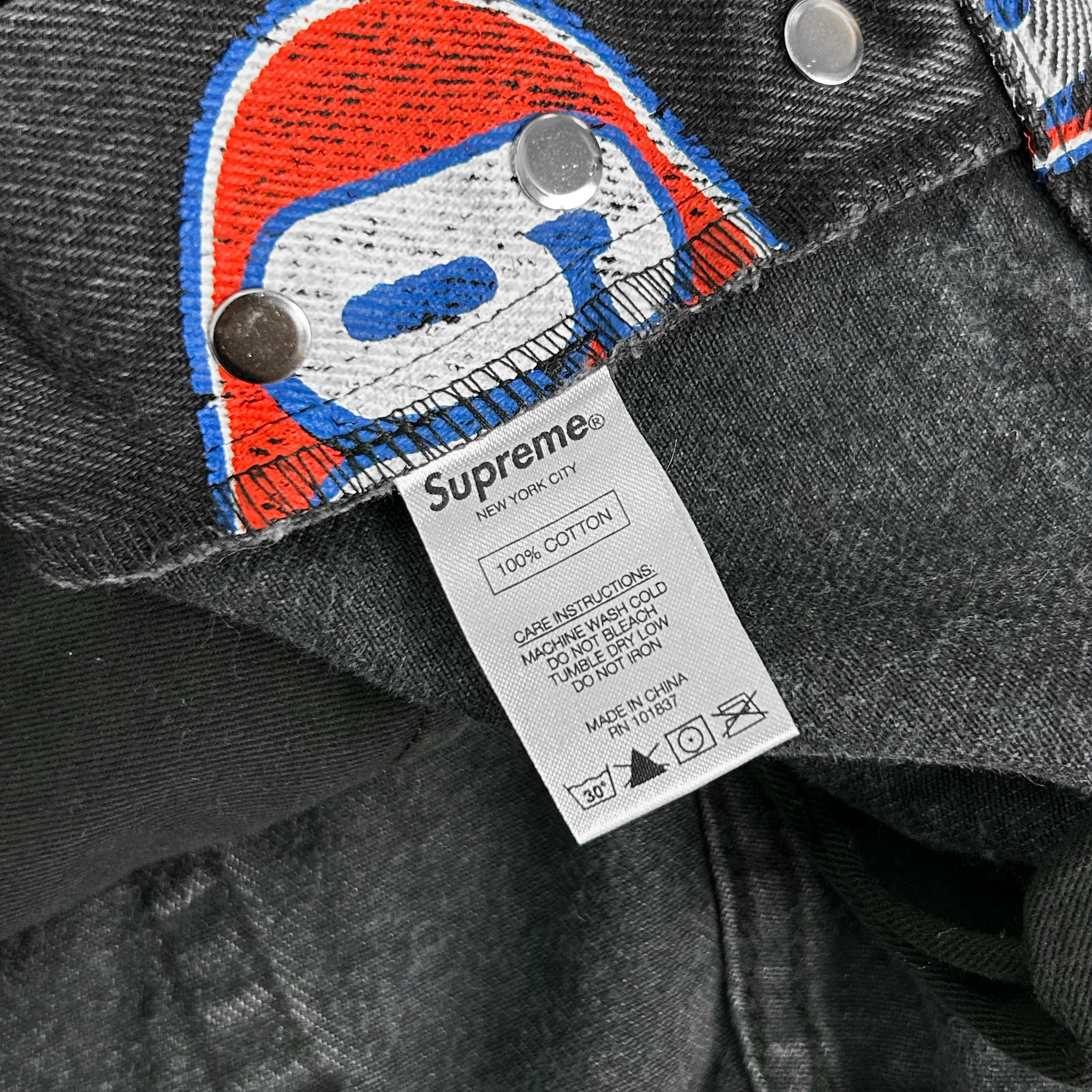 A close-up view of a denim fabric, likely a pair of jeans, with a label attached to it. The label appears to be a product label or tag, possibly indicating the brand, material, or other relevant information about the jeans.