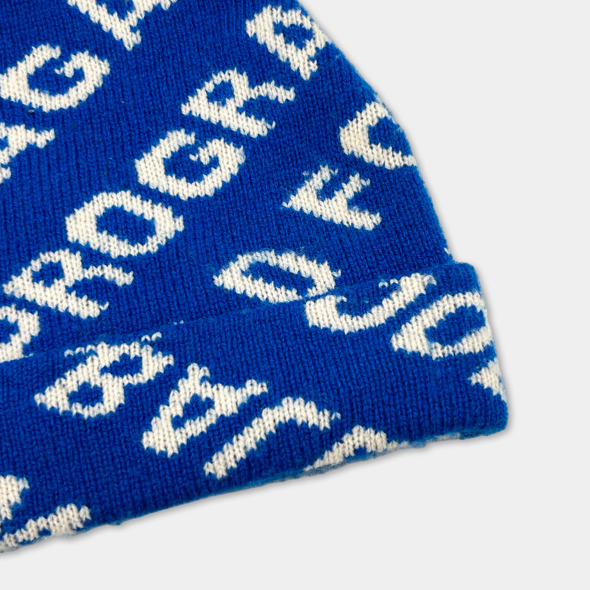 A close-up view of a blue and white knitted hat with a repeating pattern of the letters 'G' and 'R' on it.