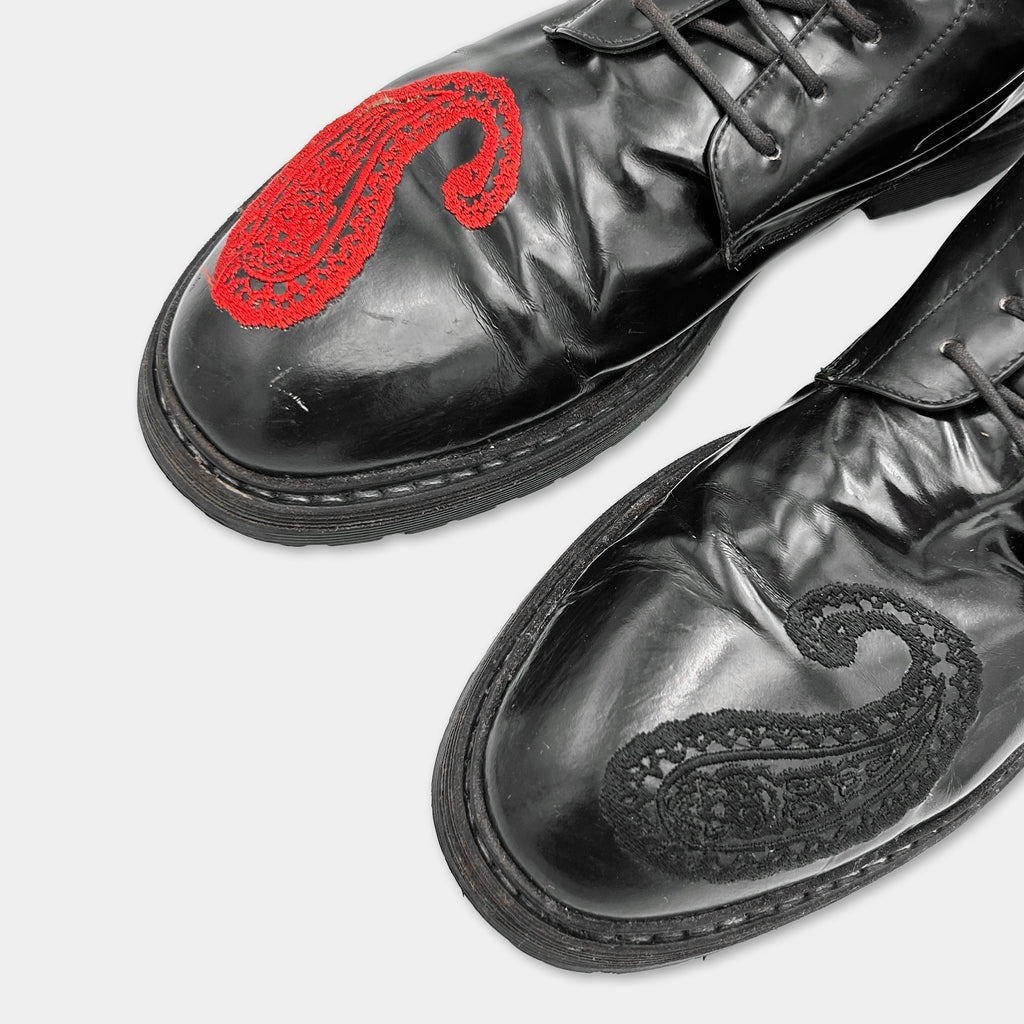 A close-up of a pair of black leather shoes with red embroidered designs on the toe and heel.