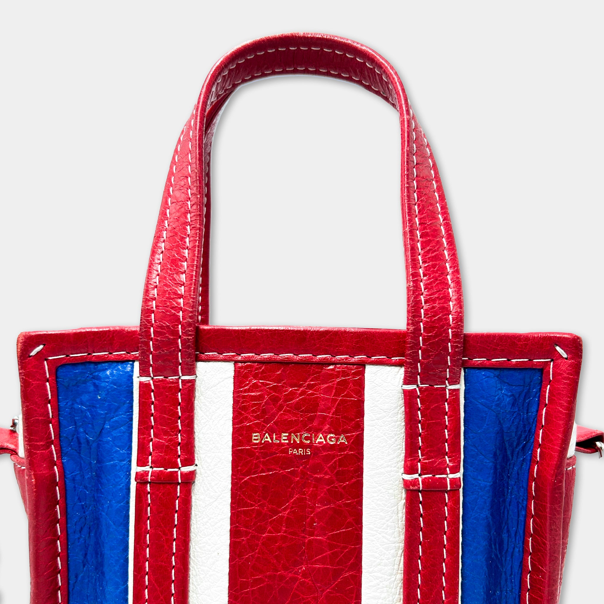 A red, white, and blue Balenciaga handbag with the brand name prominently displayed on the front.