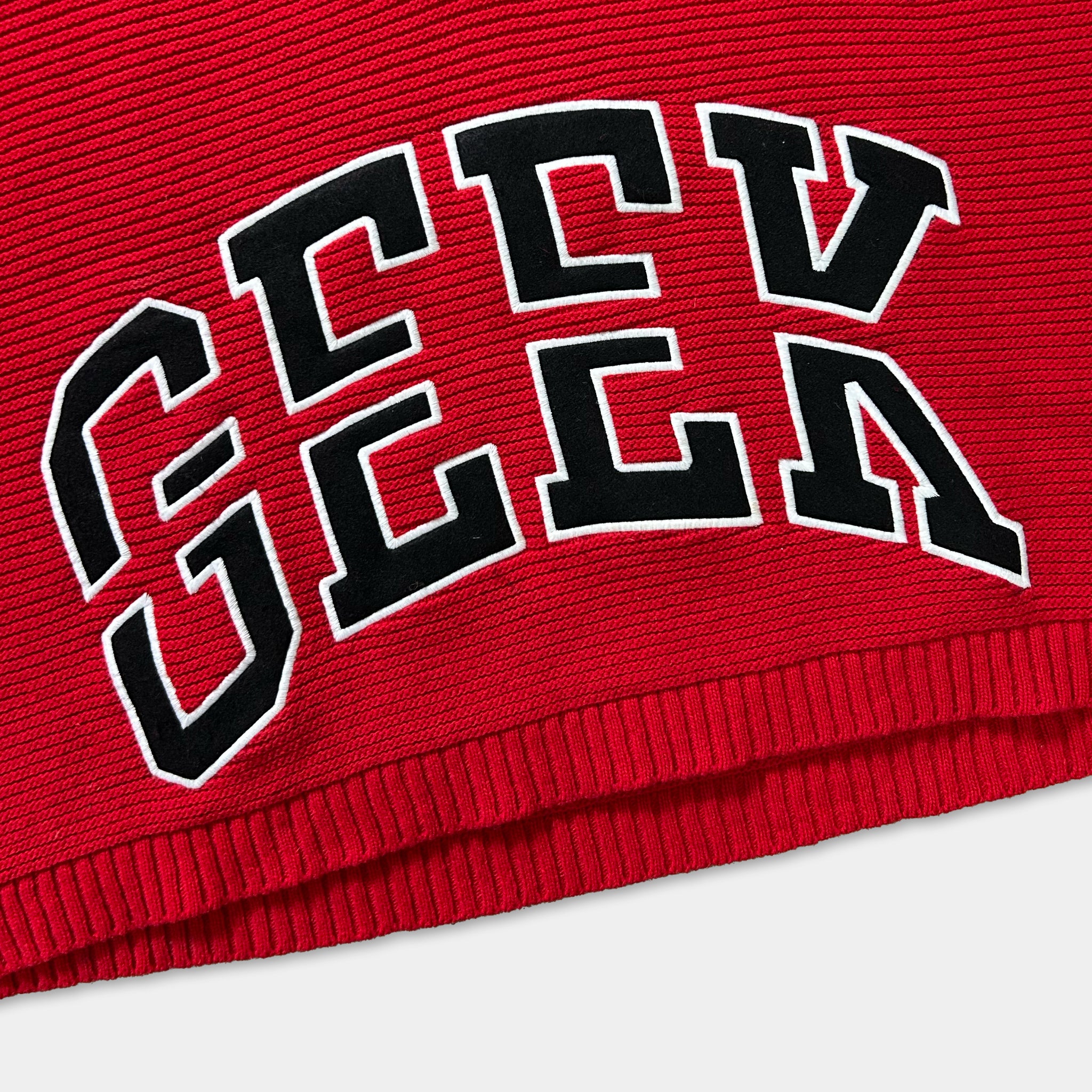 a close-up view of a red sweater with the word "GEC" prominently displayed in large, bold letters.