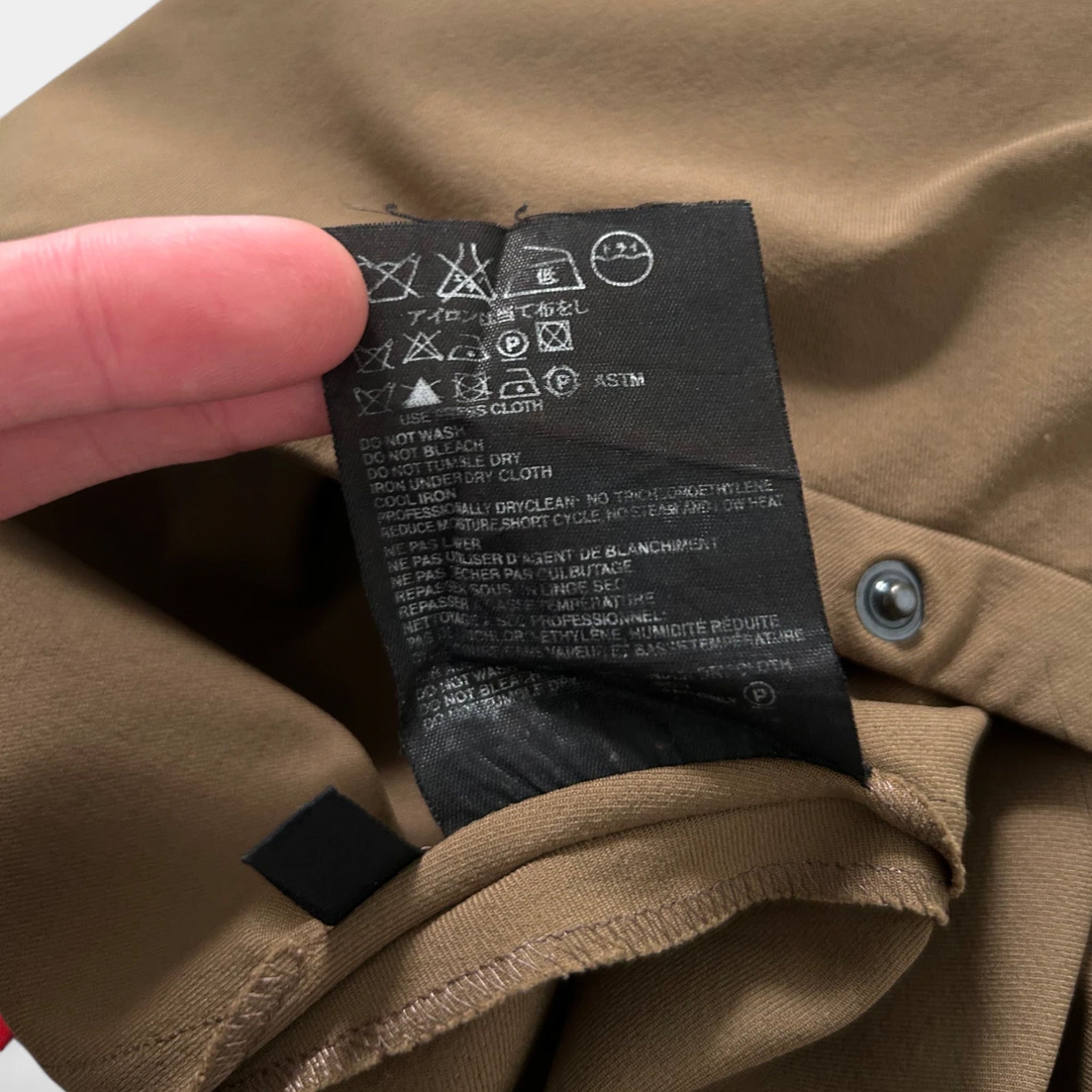 A close-up view of a black label on a beige fabric, with a person's finger pointing to it.