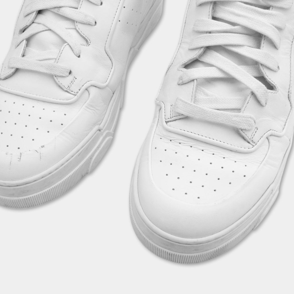 A close-up view of a pair of white sneakers with visible laces and soles.