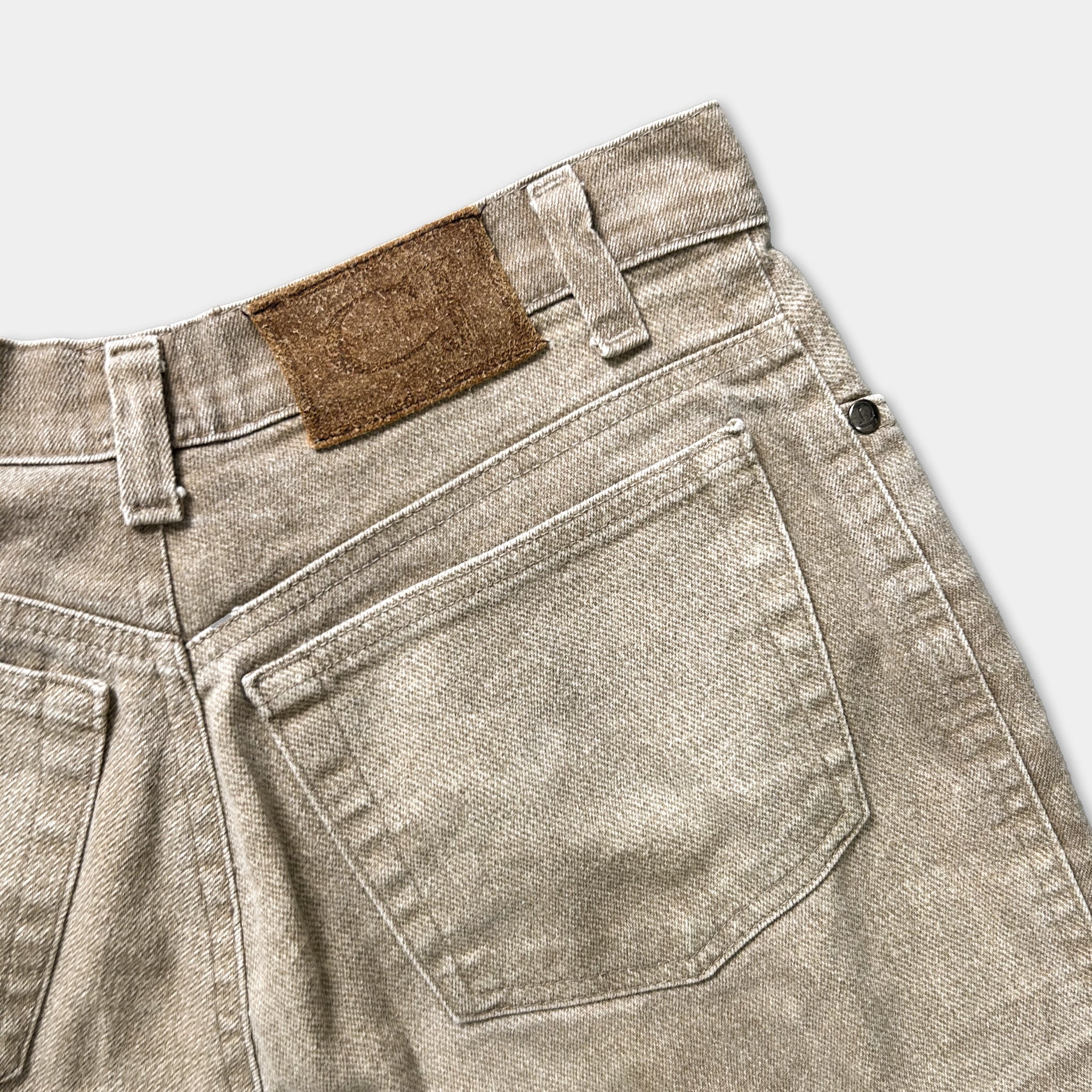 A pair of tan-colored jeans with a brown leather patch on the back pocket.