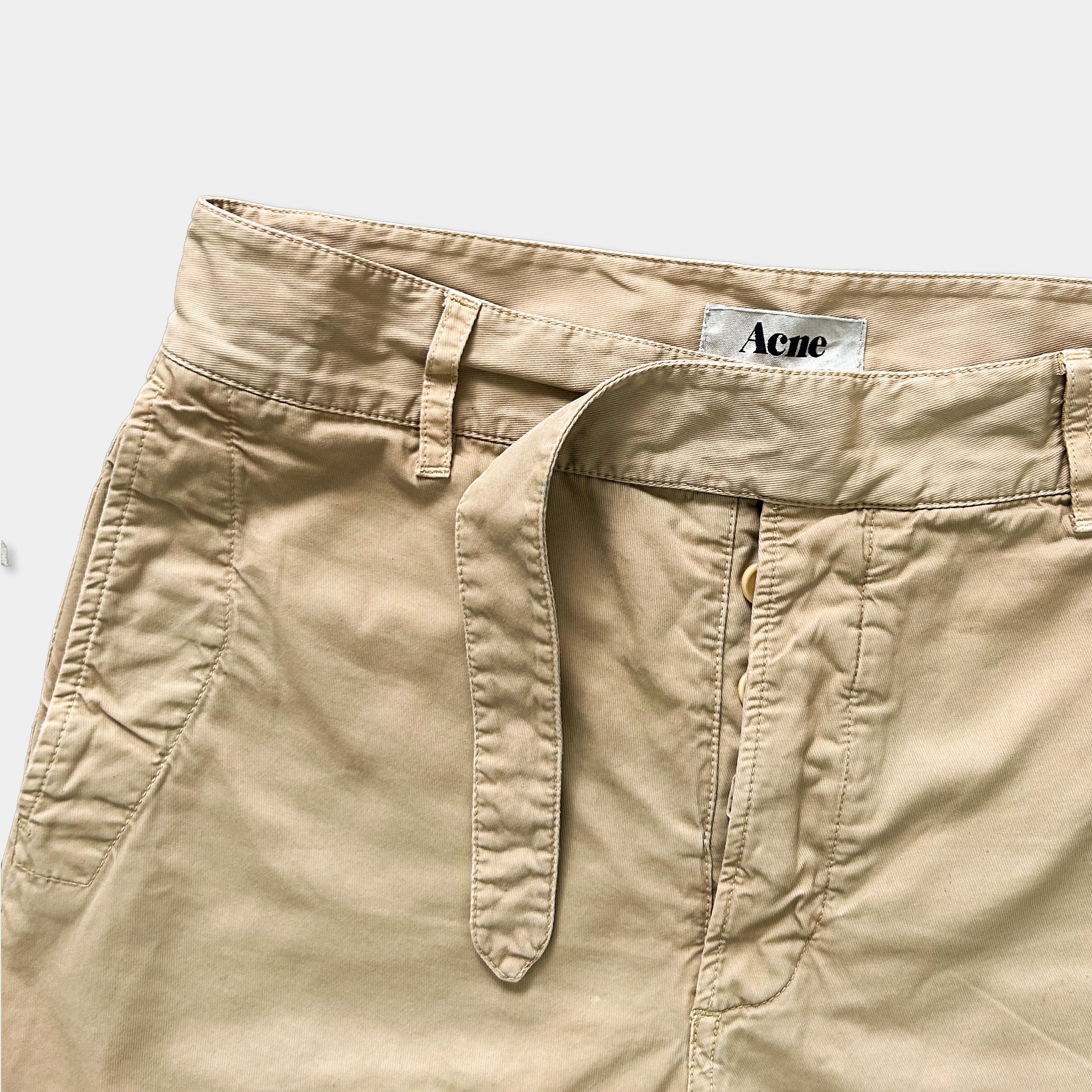A pair of khaki cargo shorts with a belt and a label on the waistband.