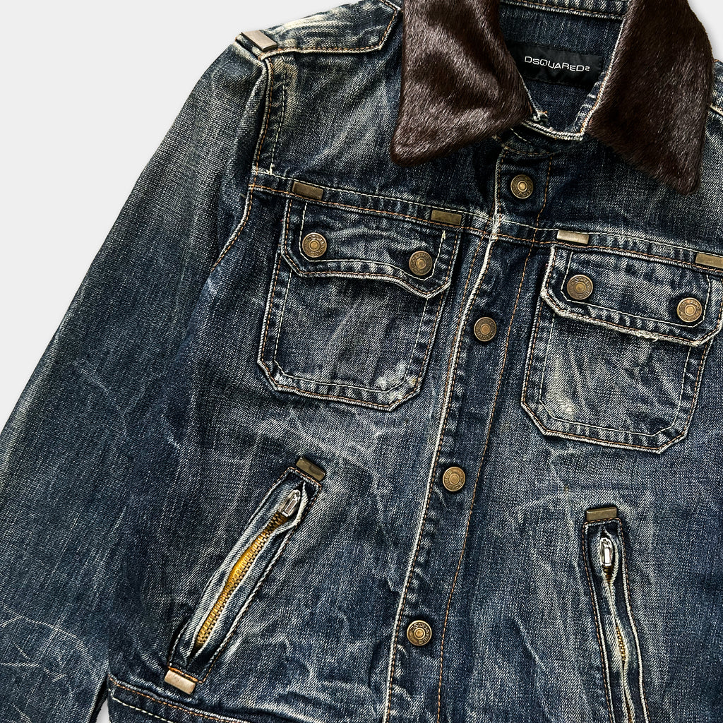 A close-up view of a blue denim jacket with a brown fur collar, showing the buttons, zipper, and pockets.