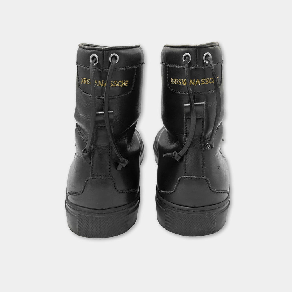 A pair of black leather boots with the name 'KRISNAASSCHE' printed on them.
