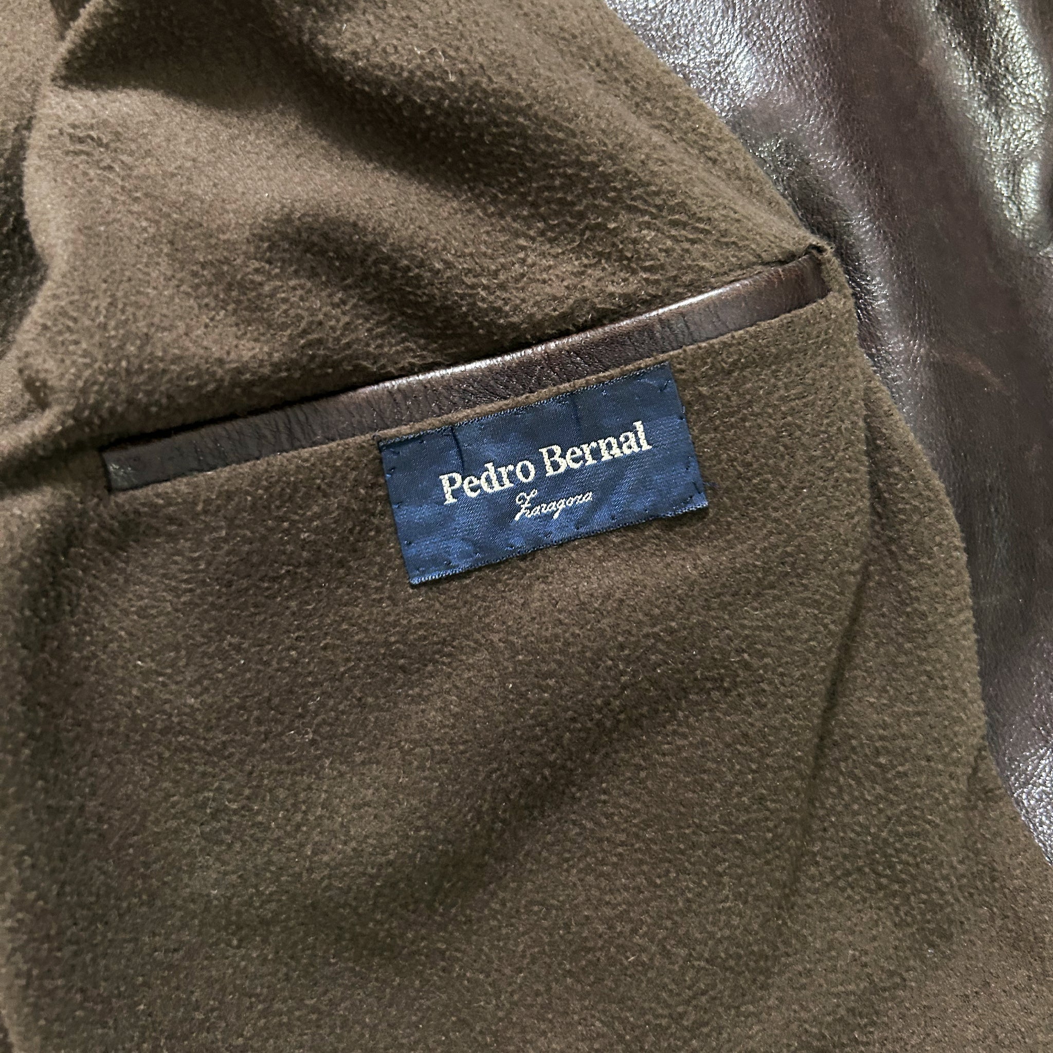 a close-up view of a brown leather jacket, with a label attached to the pocket.