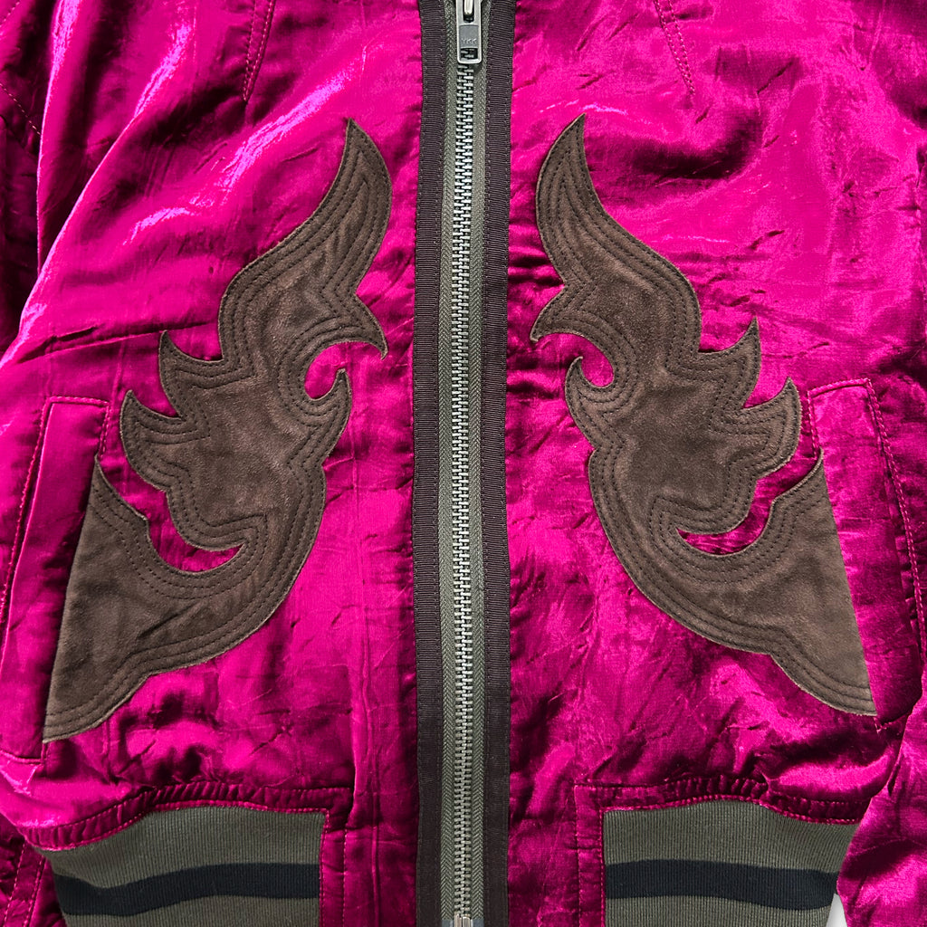 a close-up view of a vibrant pink velvet jacket with a zipper and decorative brown accents.