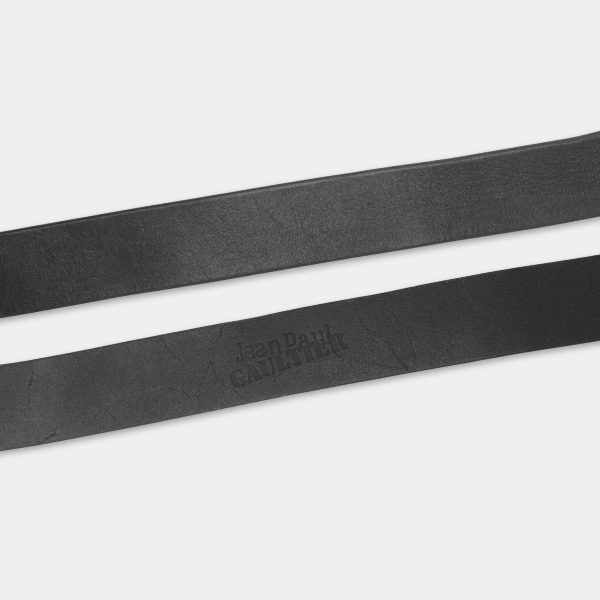 A close-up view of a black leather belt with the text "Jean Paul Gaultier" printed on it.