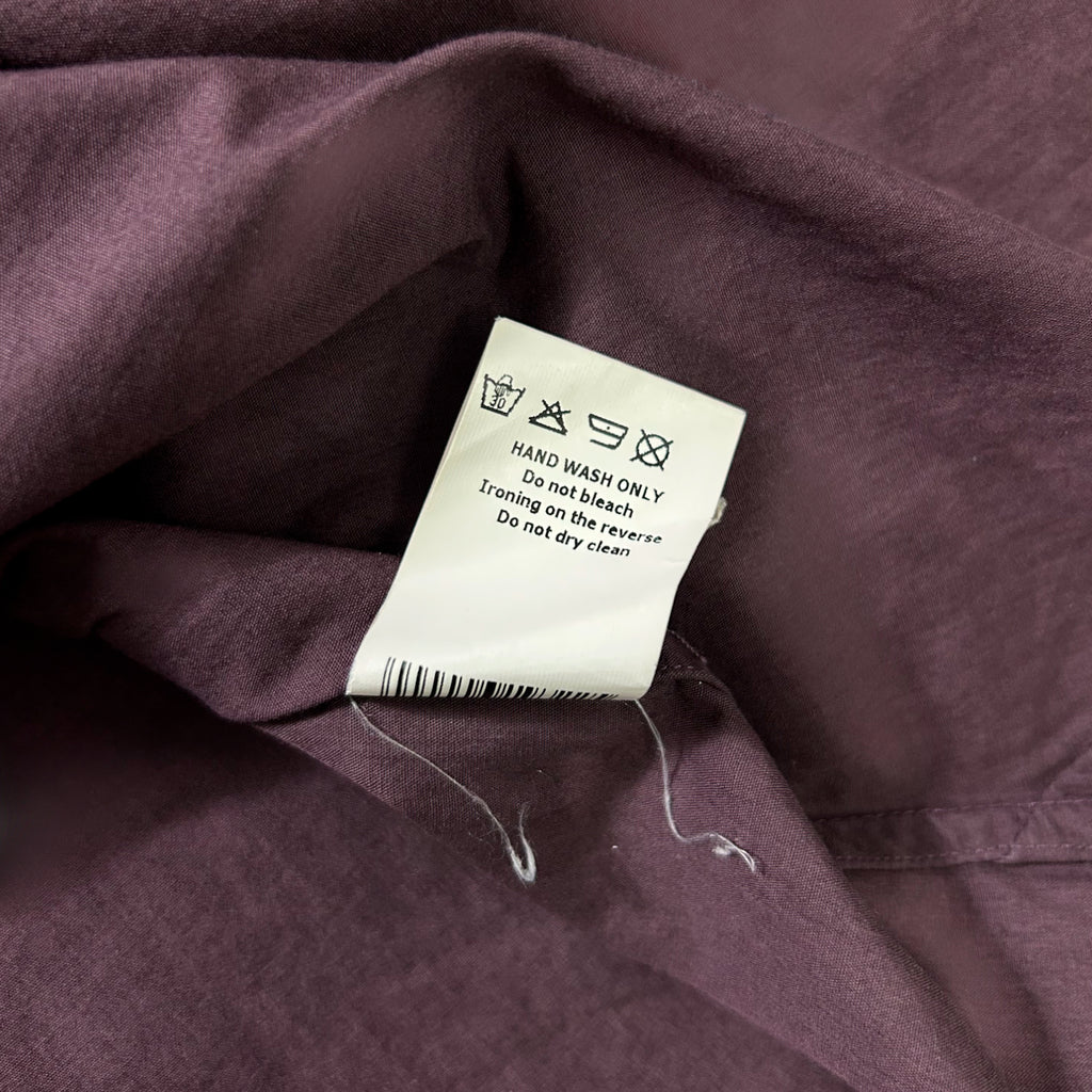 a close-up view of a purple fabric with a white label attached to it, which contains instructions for washing the fabric.