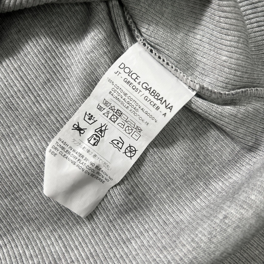 a close-up of a white label with text and symbols attached to a gray fabric, likely a garment or textile.