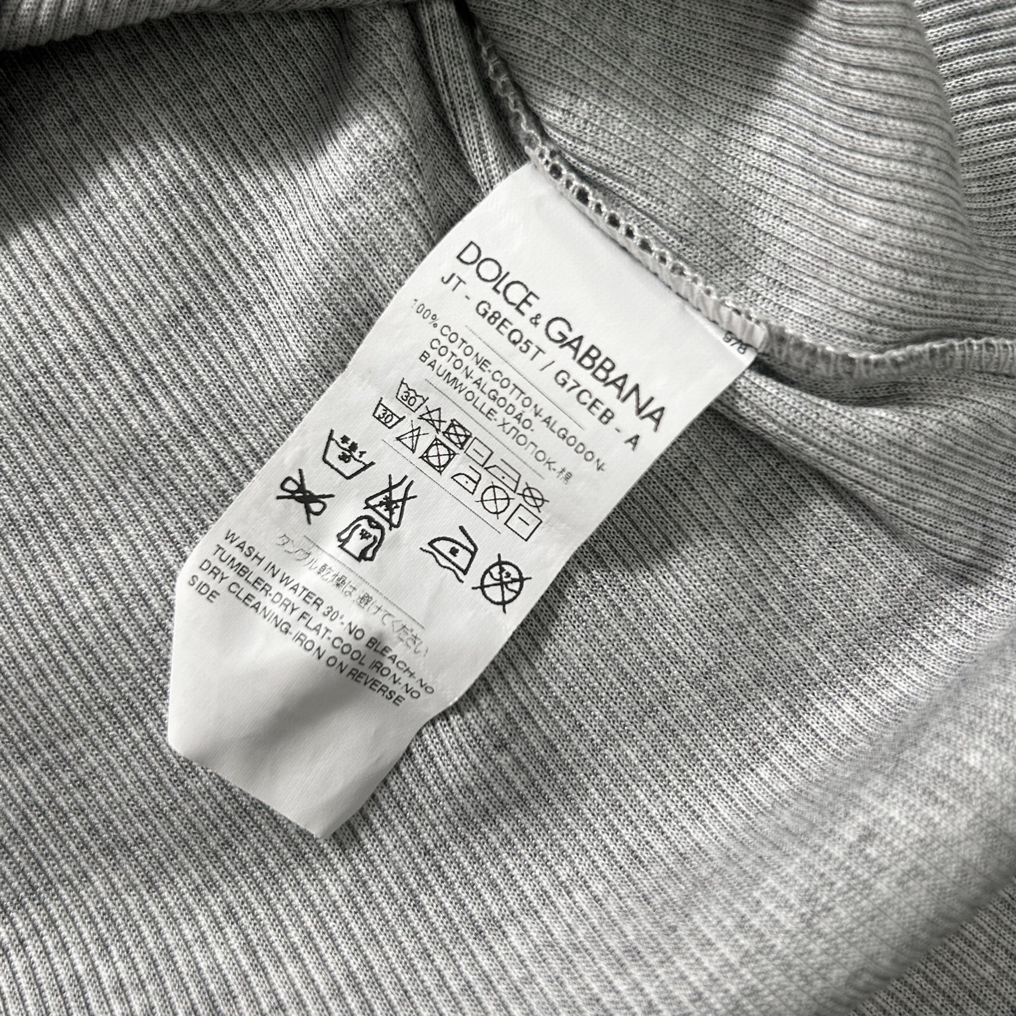 a close-up of a white label with text and symbols attached to a gray fabric, likely a garment or textile.
