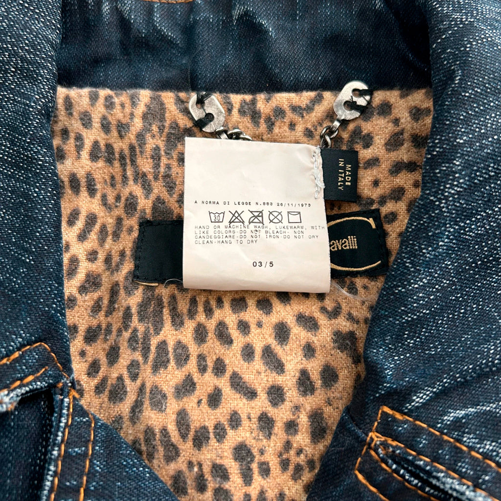 a close-up view of a denim jacket with a leopard print pattern, featuring a label attached to the collar.