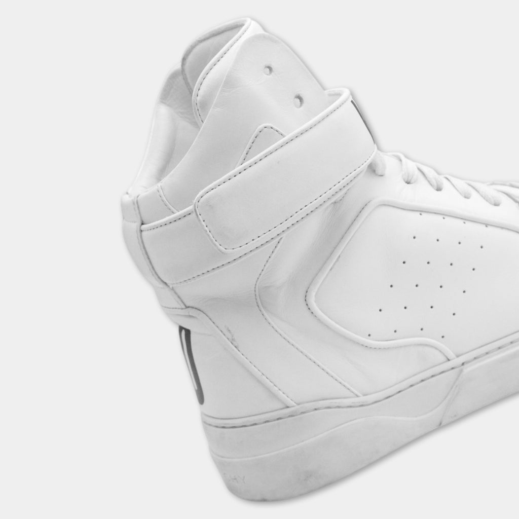 A close-up view of a white high-top sneaker with a strap across the top.