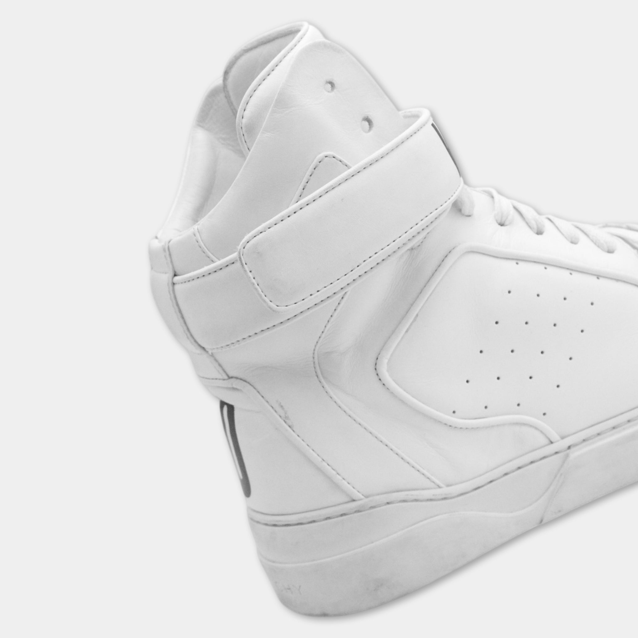 A close-up view of a white high-top sneaker with a strap across the top.