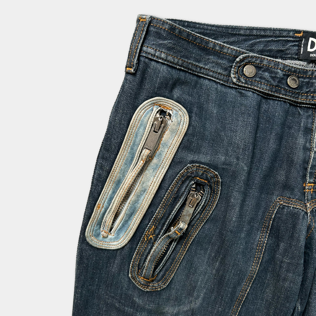 A pair of blue jeans with two zippers on the front, one larger zipper and one smaller zipper, positioned on the side of the jeans.