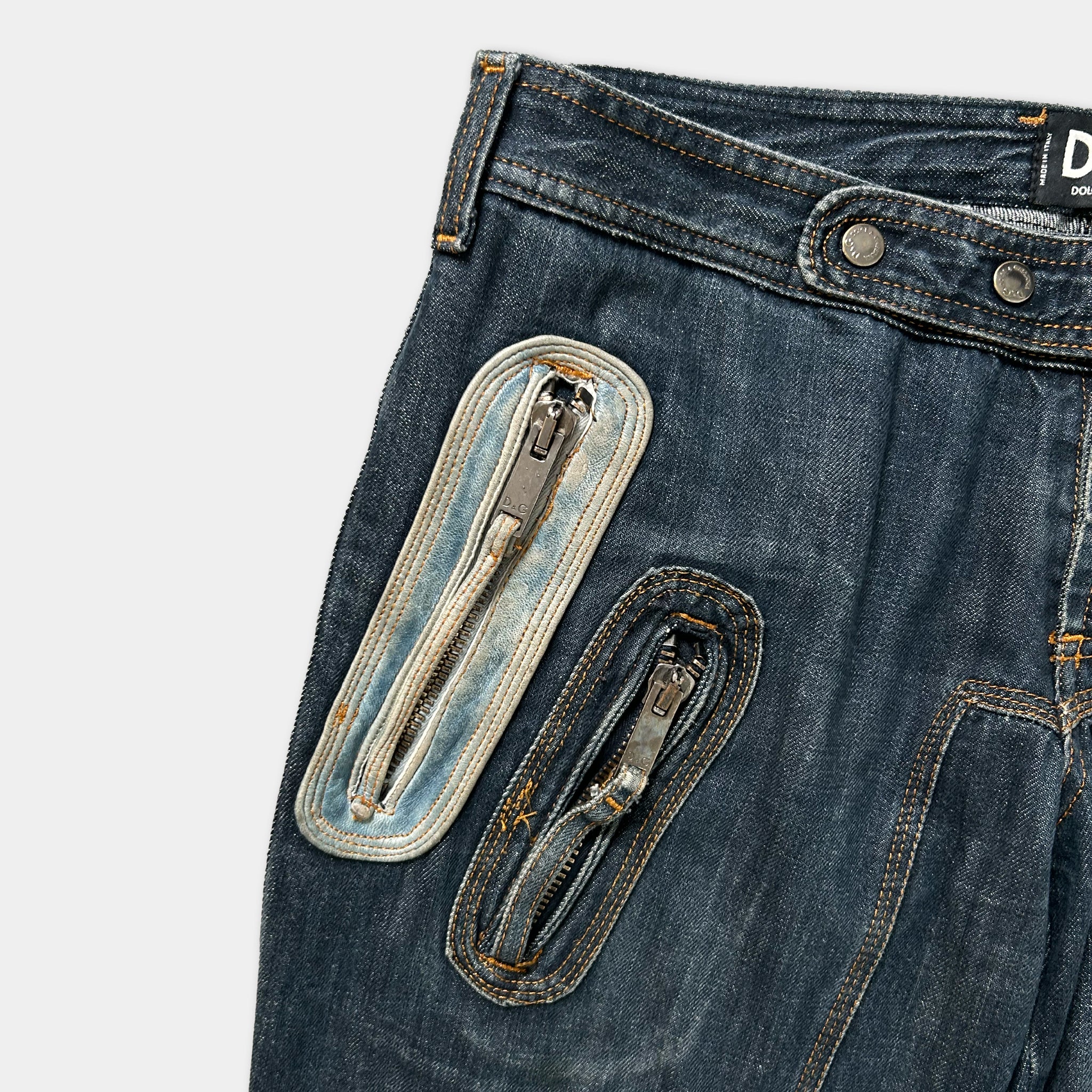 A pair of blue jeans with two zippers on the front, one larger zipper and one smaller zipper, positioned on the side of the jeans.
