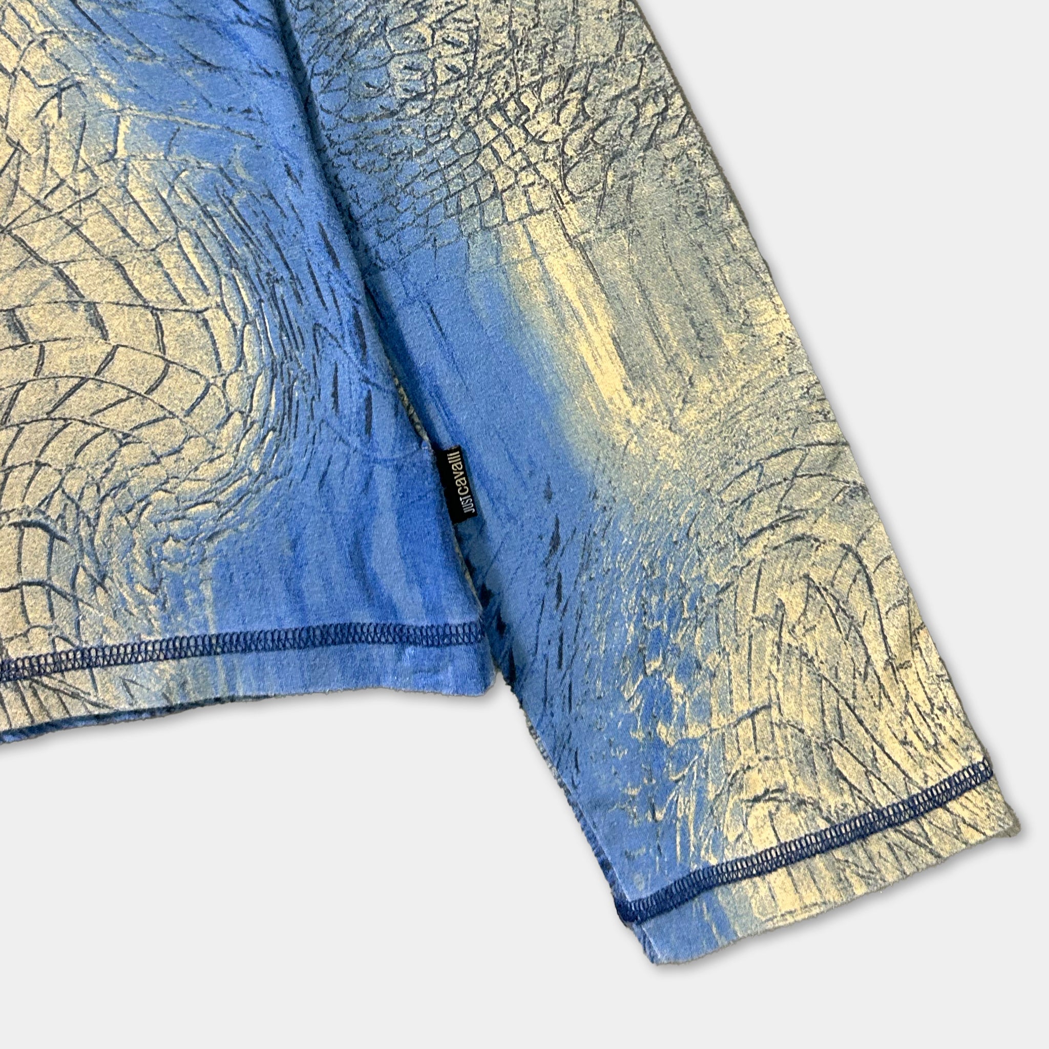 a close-up view of a blue and gold patterned fabric, possibly a shirt or garment, with a small black label attached to the sleeve.