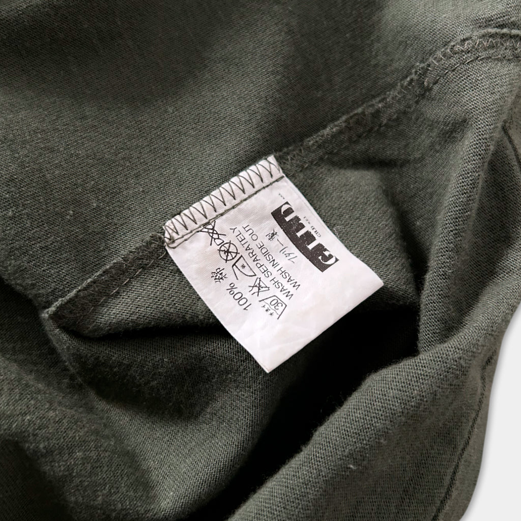 a close-up view of a dark green fabric, possibly a t-shirt or garment, with a white label attached to it. The label appears to contain text and symbols, but the exact wording is not clearly visible.