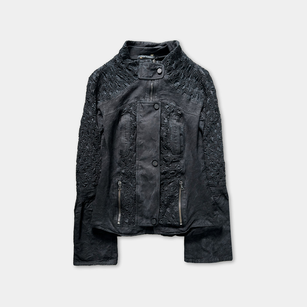 A black leather jacket with intricate embroidered details and multiple zippers.