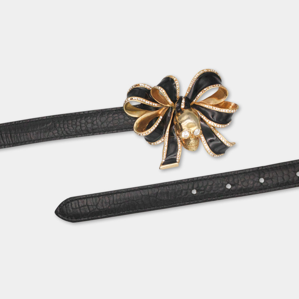 A black leather belt with a decorative gold bow and a skull-shaped embellishment on it.