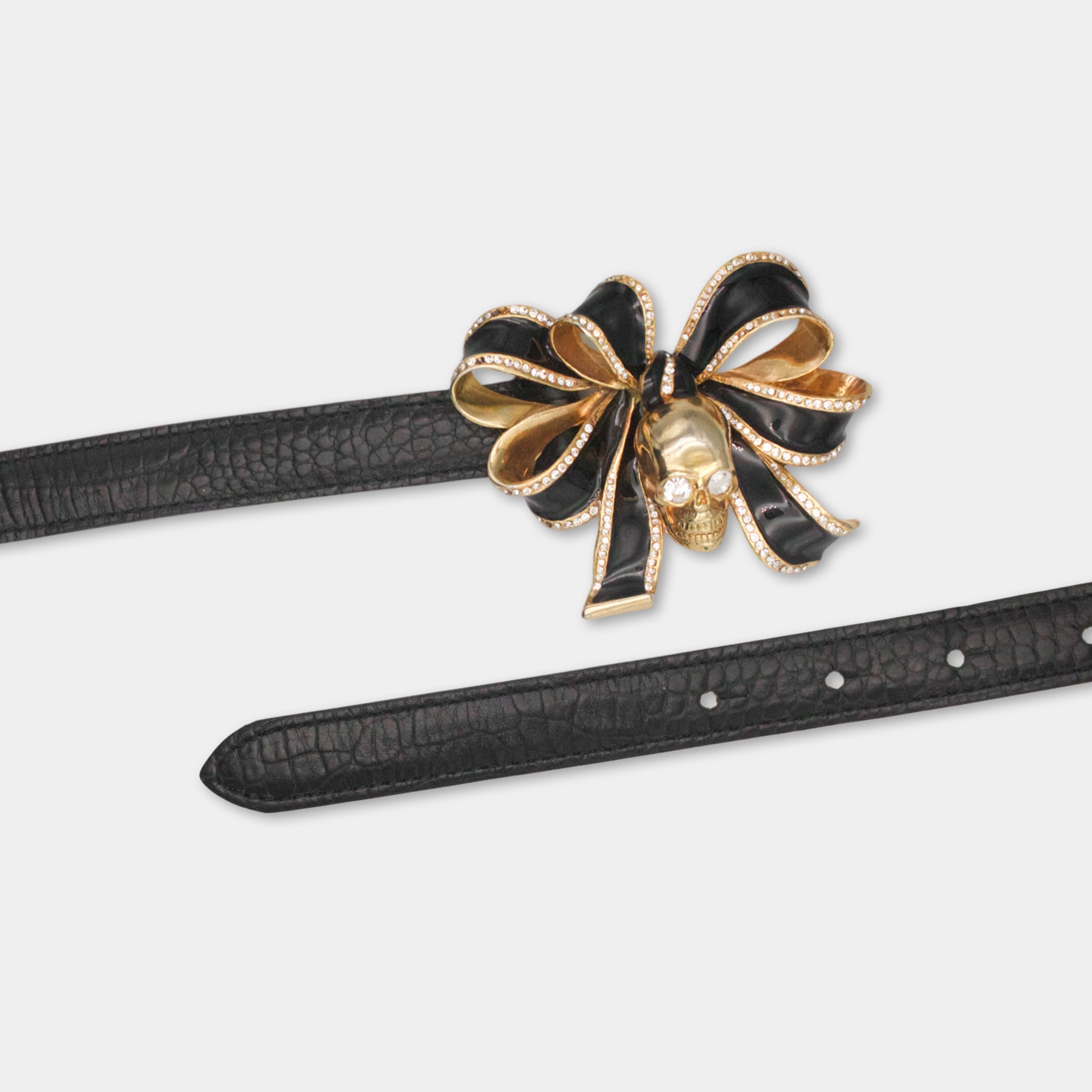 A black leather belt with a decorative gold bow and a skull-shaped embellishment on it.