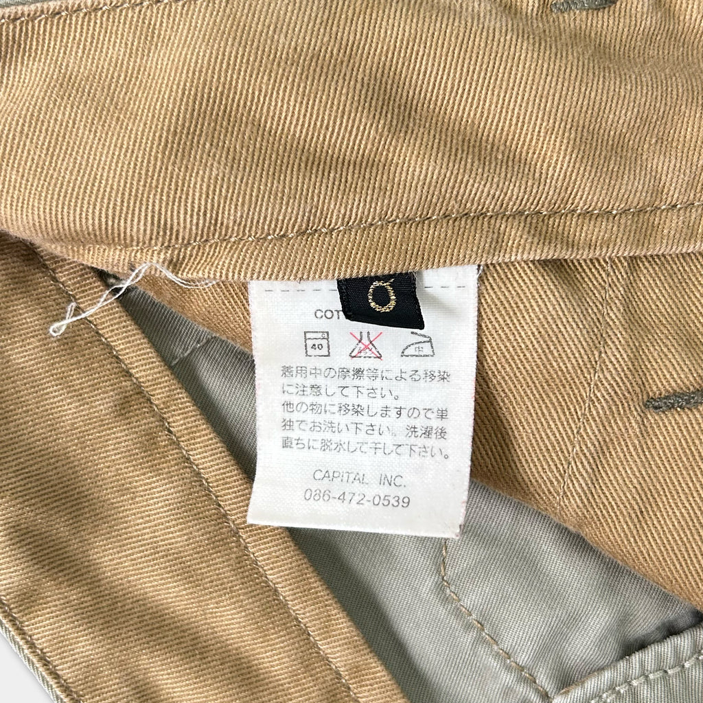 a close-up view of a beige fabric, possibly a piece of clothing, with a label attached to it. The label contains text in Japanese and English, providing information about the fabric, care instructions, and the manufacturer's contact details.