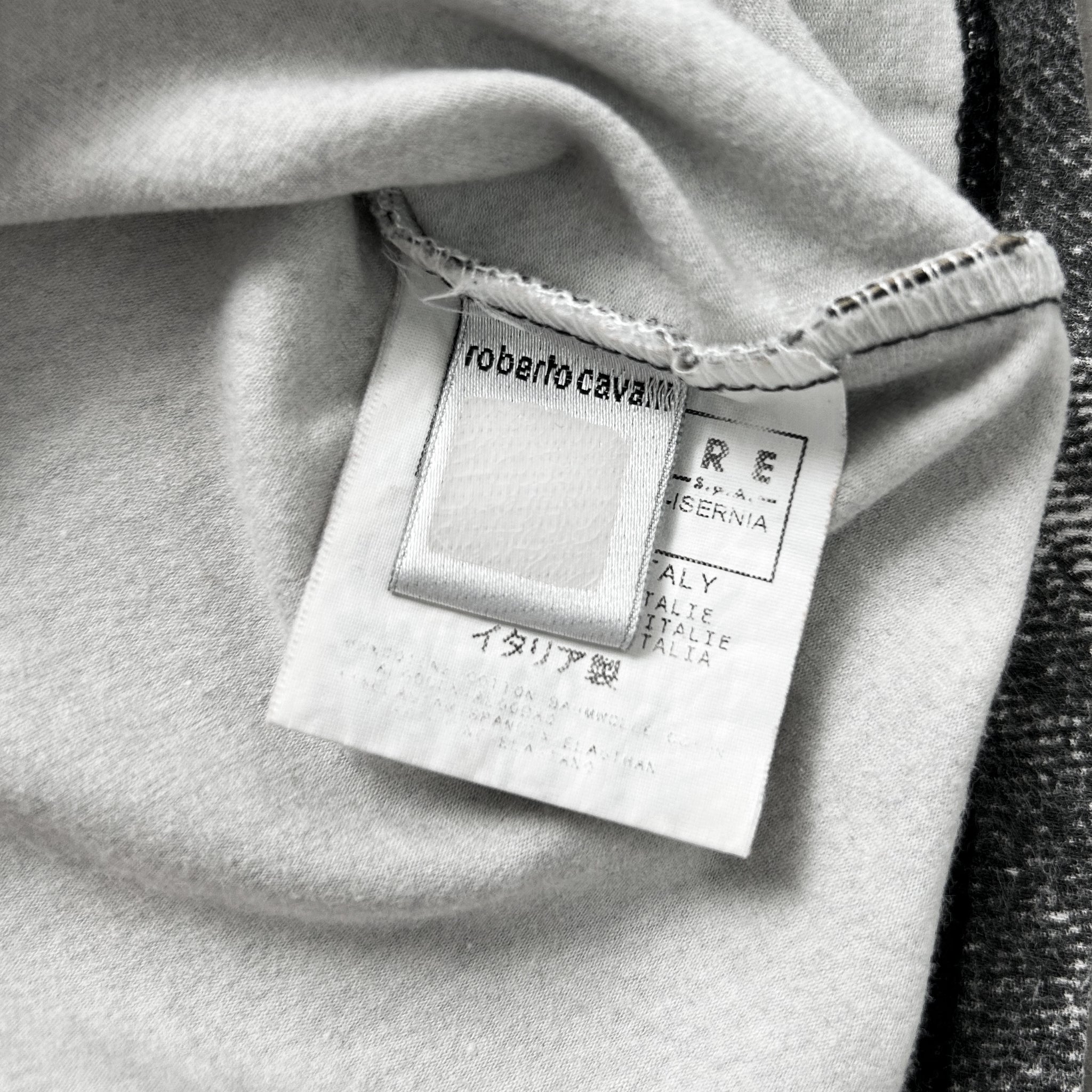 A close-up black and white image of a fabric label with text and logos, including the brand name and country of origin.
